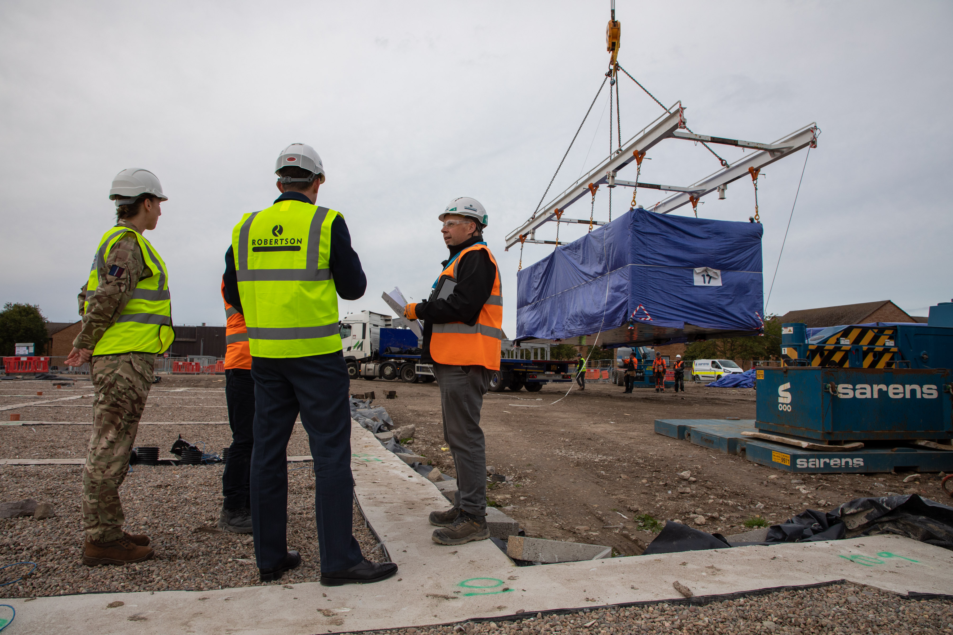 Image shows RAF aviators and civil servants on construction site with a crane lifting crates.